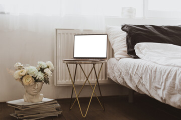 Working at home concept. Laptop computer with white screen in bed with white linens. Minimalistic cozy home workspace background.