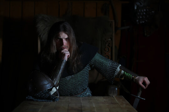 A mighty hero with long hair in chain mail armor in an ancient hall. Medieval warrior in the knight's chambers.