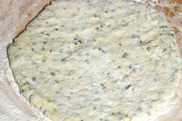 Dough rolled out on a wooden board for flatbread with onion cheese and beacon.