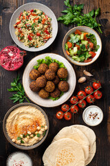 Middle eastern or arabic cuisines, falafel, hummus, tabouleh, pita and vegetables on wooden background, view from above