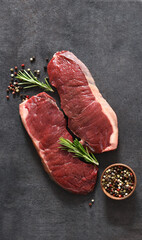 Steak, raw beef with spices and rosemary on a black concrete background. View from above.