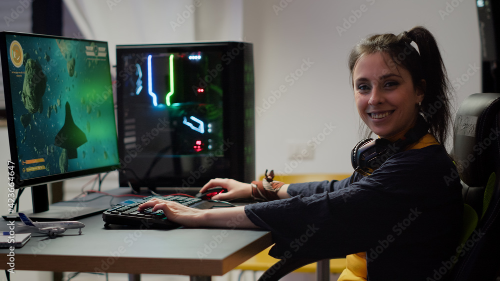 Wall mural Portrait of concentrated gamer looking at camera smiling, playing online space shooter video game for gaming tournament. Cyber performing on powerful pc with RGB keybord streaming video games