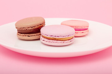 three macaroons on white plate on pink paper background. Sweet bakery, copy space. Overweight, diet, diabetes, healthy eating habits.