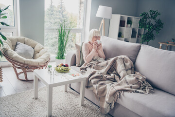 Portrait of nice sick elderly grey-haired woman lying on divan sneezing feeling bad in house flat...