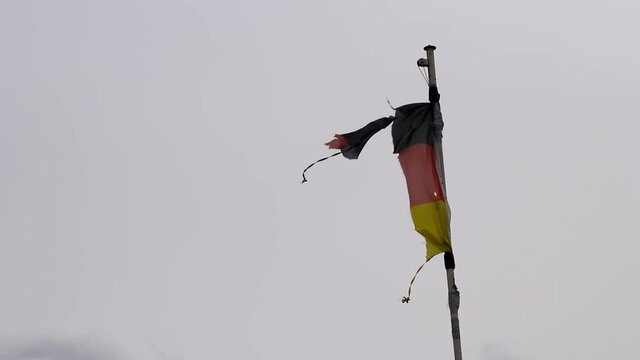 Tattered German flag  waving demolished and destroyed in windy times in national crisis with the threat of bankrupt instead of glory with political crisis as well as financial stumble and inflation