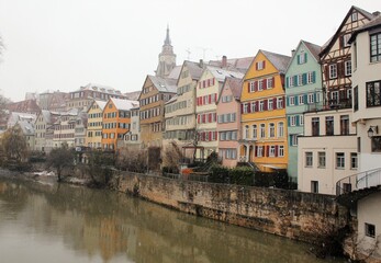 Fototapeta na wymiar Neckar front on a snowy winter day in Tübingen, Baden-Württemberg, Germany. Beautiful landscape with colorful houses and a light snowfall 