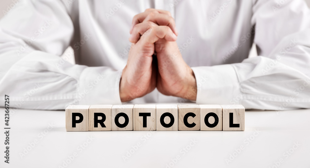 Poster the word protocol written on a wooden block in front of a businessman with crossed hands.