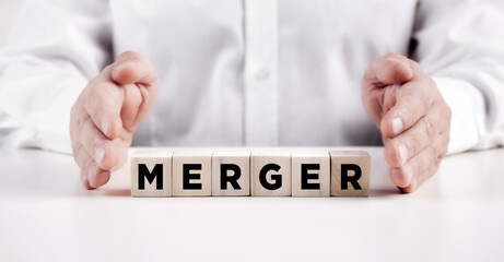 Businessman hands covers the wooden cubes with the word merger.