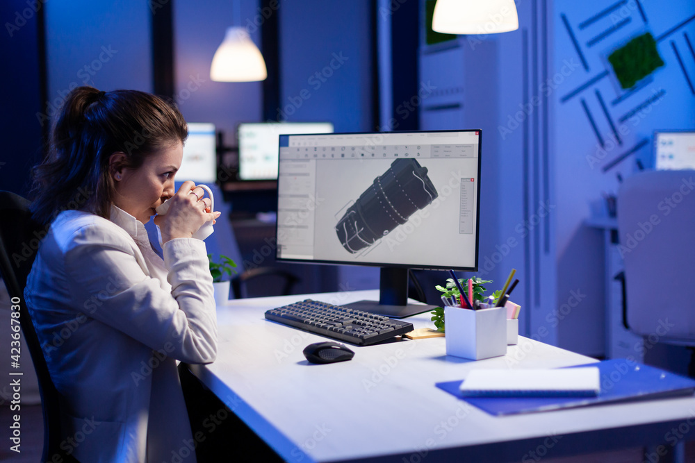 Poster woman engineer working late at night on 3d model of industrial turbine while drinking coffee in fron