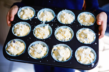Overhead view of a baking tray with freshly prepared plain blueberry muffins holding by a child