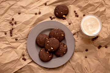 Baked dark Chocolate chip cookies on a plate with glass of coffee on brown paper background