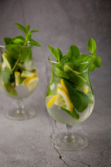 Summer mint lime refreshing cocktail mojito with rum and ice in glass on gray background. Mojito cocktail on stone table. Glassy high glass for drinks. Lemonade at the bar.