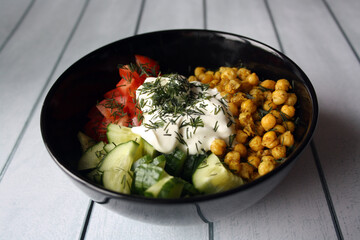 Chickpeas, tomatoes, cucumbers. Ingredients for the salad in a black bowl.