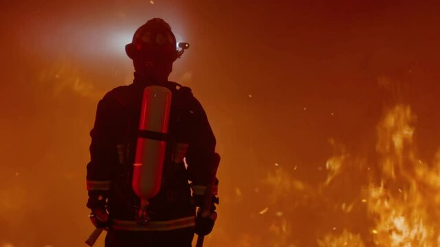 Dramatic silhouette of American firefighter in full gear exploring the huge fire zone. Shot with 2x anamorphic lens 