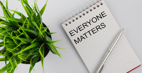 Keyword everyone matters - business concept text on a white notebook and pen, green flowers