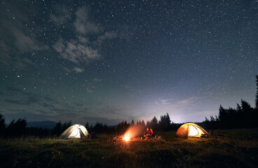Hikers standing near campfire under beautiful starry sky.