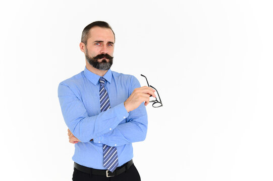Portrait of confident middle-aged businessman in blue shirt and holding glasses with a beard and mustache standing on white background with copy space