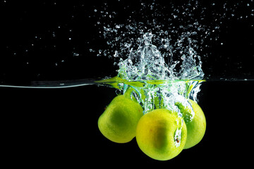 Fototapeta na wymiar Green apples falling into the water with a splash against black background
