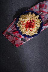 Big dinner portion of pasta with tomato sauce on blue plate, grey background. Macaroni with hot ketchup or adjika flavouring. Top view, copy space