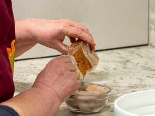 Grandmother mixing cinnamon powder in a bowl with sugar for baking a dessert. Woman hands seasoning with cinnamon in a countertop for homemade cooking.