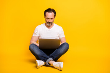 Full size photo of serious focused mature man sit floor work online freelancer isolated on yellow color background