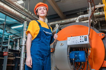Concept of a industrial manufactory. A female smiling worker in uniform and helmet with a folder in...