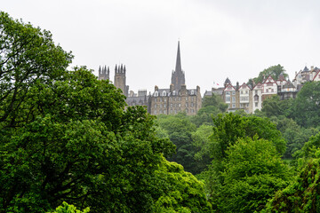 Fototapeta na wymiar Row of old historic buildings behind large green trees in Edinburgh, Scotland in a cloudy rainy summer day.