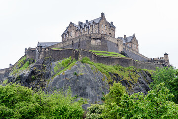 Edinburgh Castle, Scotland and old green trees, as seen from Princes Street Gardens in a cloudy rainy summer day.