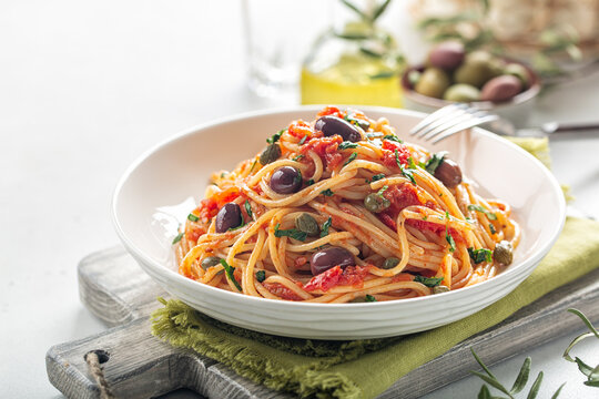 Italian lunch. Spaghetti alla puttanesca - italian pasta dish with tomatoes, olives, capers and parsley. Light background. Copy space.