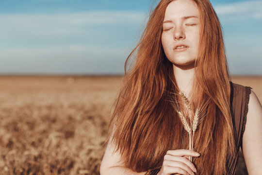 Young ginger woman in the wheat field looking relaxed.