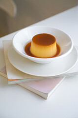 Caramel pudding dessert in a white plate placed on a book.