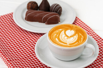 Cup of coffee and saucer with chocolate sweets on wooden table