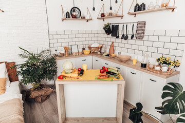 Cozy wooden apartment kitchen interior with furniture and bedroom area. Contemporary studio flat. Spacious solution of living room. Food vegetables on table. Supplies for cooking, copy space
