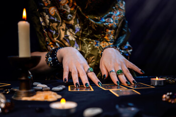 A fortune teller reads Tarot cards. On the table are candles and fortune-telling objects. Hands close up. The concept of divination, cartomancy and esotericism