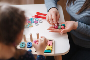 Little girl play in educational game for children with mom. Wooden game with different colors and numbers. Intecactive game for clever kids. Close up of mother's hand give daughter color balls