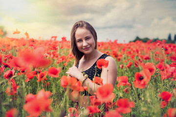 Young slim woman in black short top in field with blooming poppies