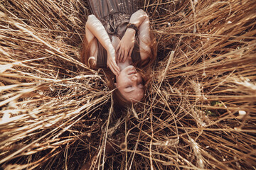Young ginger woman in the wheat field looking relaxed.