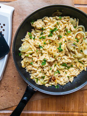 Spaetzle or Spätzle egg noodle pasta with onions, parsley and seasoning in a pan. Traditional European cuisine dish (Swabian, German, Austrian). Handmade gluten free Knöpfle. Grater in background