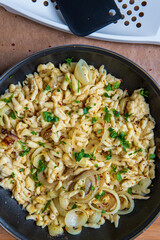 Spaetzle or Spätzle egg noodle pasta with onions, parsley and seasoning in a pan. Traditional European cuisine dish (Swabian, German, Austrian). Handmade gluten free Knöpfle. Grater in background