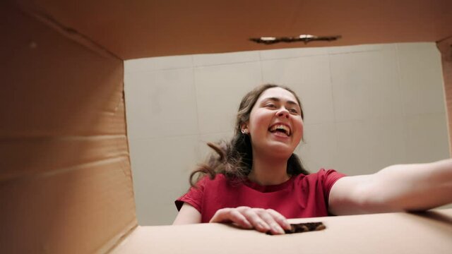 Unpacking. A young happy woman opens a cardboard box and excitedly takes out a laptop. Bottom view. Product delivery and movement concept.