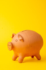 Close-up clay piggy bank, yellow background, vertical, with copy space