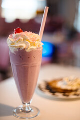 Delicious sweet cherry milkshake with whipped cream on table.