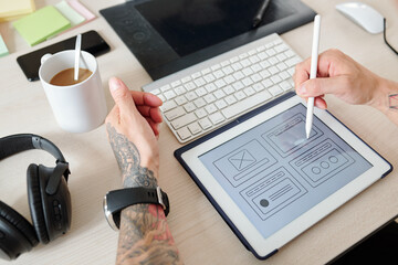Hands of UI designer working on interface of new website or mobile application, he is pointing at...