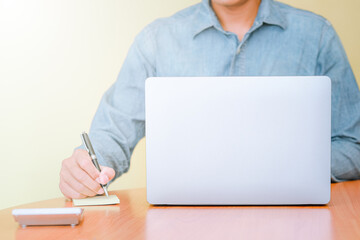 A businessman using a laptop computer to search for information and take notes on paper.