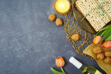 Jewish holiday Passover background with matzah, seder plate, wine and tulip flowers on dark table