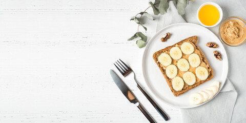 Homemade peanut butter sandwich with bananas and honey on wooden background.