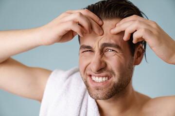 Shirtless white man squeezing out pimple and looking at camera