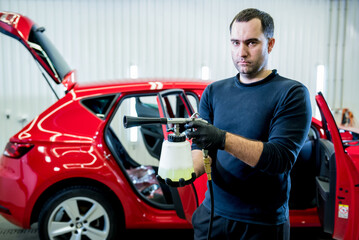 Fototapeta na wymiar A car service worker cleans interiror with a special foam generator
