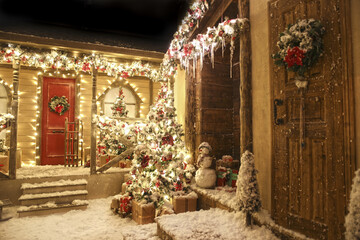 Fototapeta premium Realistic decorated studio Christmas Street with two adjacent houses with icicles, porch, doors with wreaths, Christmas trees, snowman, a sleigh and fake sno