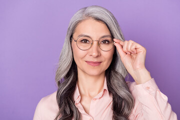 Portrait of attractive trendy intellectual cheery woman touching eyewear isolated over violet purple color background